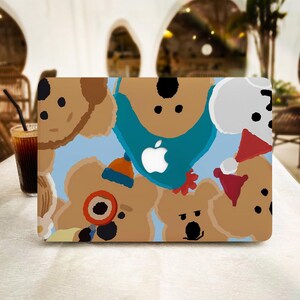 May include: A laptop case featuring a whimsical pattern of cartoon koala bears in various outfits. The design includes a light blue background with a white Apple logo. The koalas are in shades of brown, with accents of blue, orange, and red.