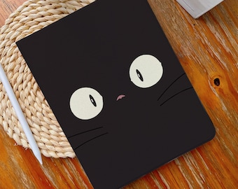 May include: Black tablet case featuring a cartoon cat face with large, round eyes and whiskers. The case is rectangular and appears to be made of a smooth material. The cat's eyes are off-white with black pupils, and the nose is a small pink shape.