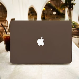 May include: A brown laptop computer with a white Apple logo on the lid. The laptop is sitting on a white surface.