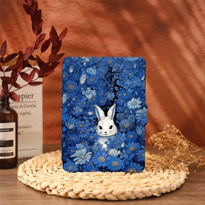 Può includere: Una custodia per telefono con motivo floreale blu e bianco con un coniglio bianco che spunta dai fiori.