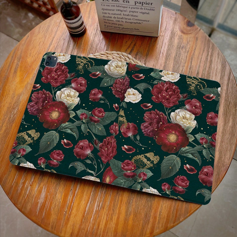 May include: A dark green laptop skin with a floral pattern featuring red, white, and gold butterflies. The flowers are red, white, and pink with green leaves.