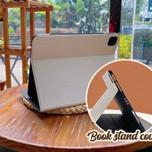 May include: A white and black tablet case with a stand feature. The case is folded to create a stand for the tablet. The text "Book stand cover" is visible in the image.
