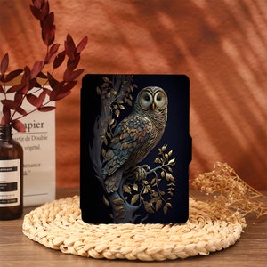 May include: A black e-reader case featuring a gold and blue owl illustration. The owl is perched on a branch with gold leaves.