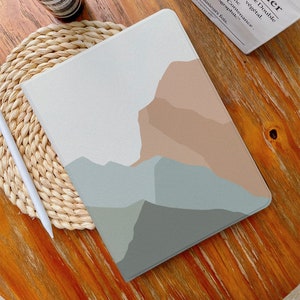 May include: A white iPad case with a minimalist abstract design featuring a mountain range in shades of brown, beige, and blue.
