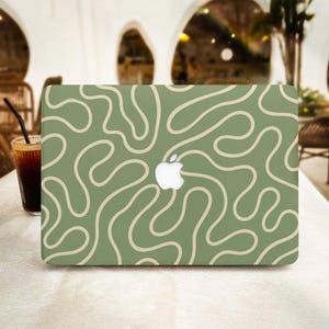 May include: A laptop skin featuring a sage green background with a continuous, winding cream-coloured line pattern that curves across the surface, centred around the white Apple logo cutout on the lid of the closed laptop device.
