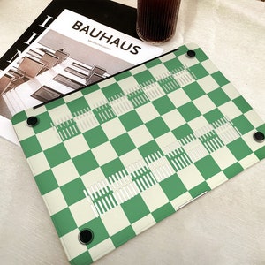 Puede incluir: Piel de port&aacute;til a cuadros verde y blanco con una revista Bauhaus en el fondo.