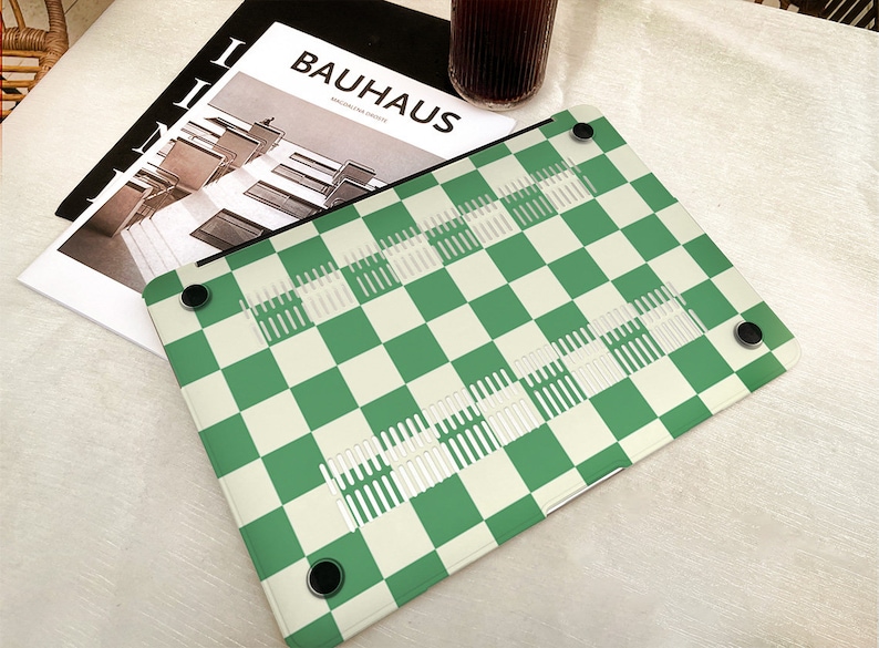 Puede incluir: Piel de port&aacute;til a cuadros verde y blanco con una revista Bauhaus en el fondo.