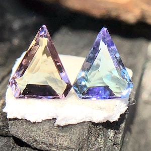 May include: Two triangular faceted gemstones, one is a pale yellow with purple hues and the other is a light blue with purple hues.