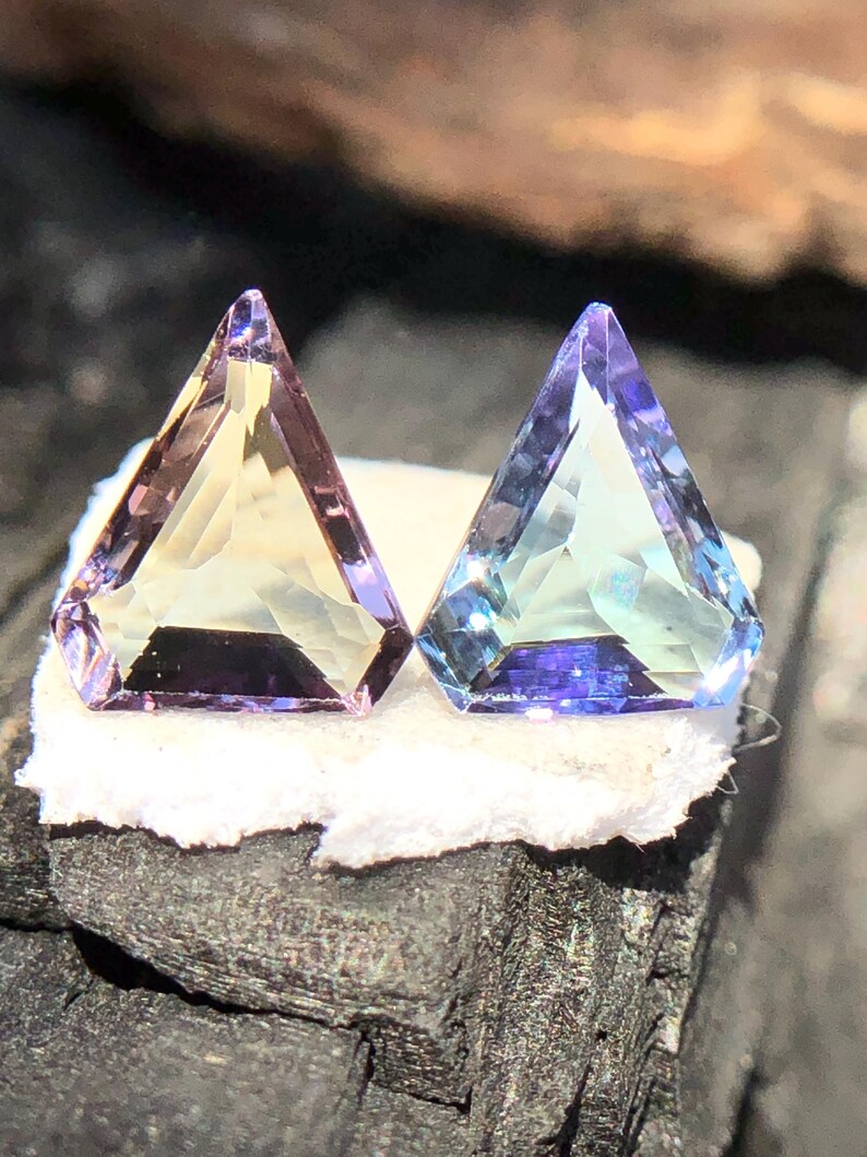 May include: Two triangular faceted gemstones, one is a pale yellow with purple hues and the other is a light blue with purple hues.