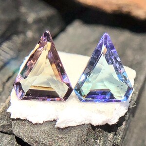 May include: Two triangular faceted gemstones, one is a pale yellow with purple hues and the other is a light blue with purple hues.