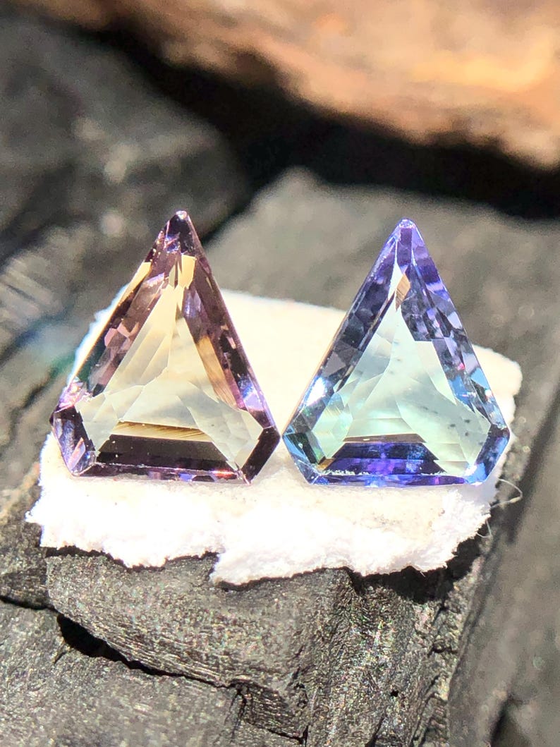 May include: Two triangular faceted gemstones, one is a pale yellow with purple hues and the other is a light blue with purple hues.