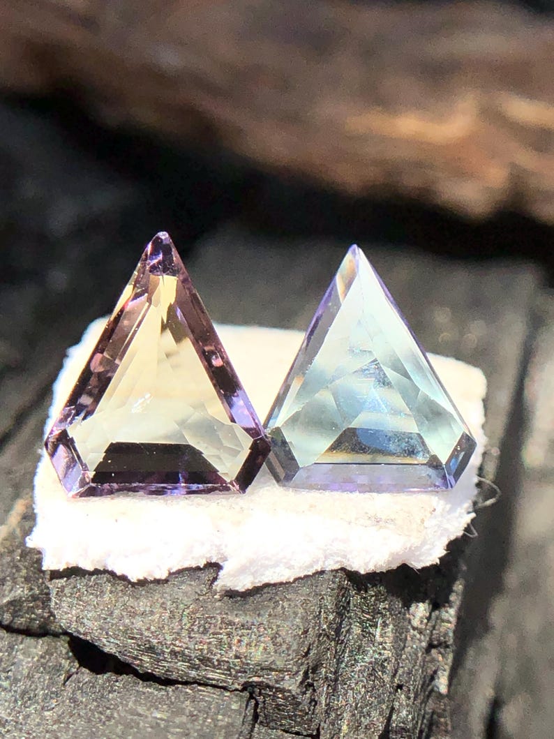 May include: Two faceted gemstones, one is a light purple and yellow, the other is a light blue and purple.