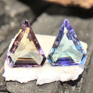 May include: Two triangular faceted gemstones, one with a purple and yellow hue and the other with a blue and green hue.