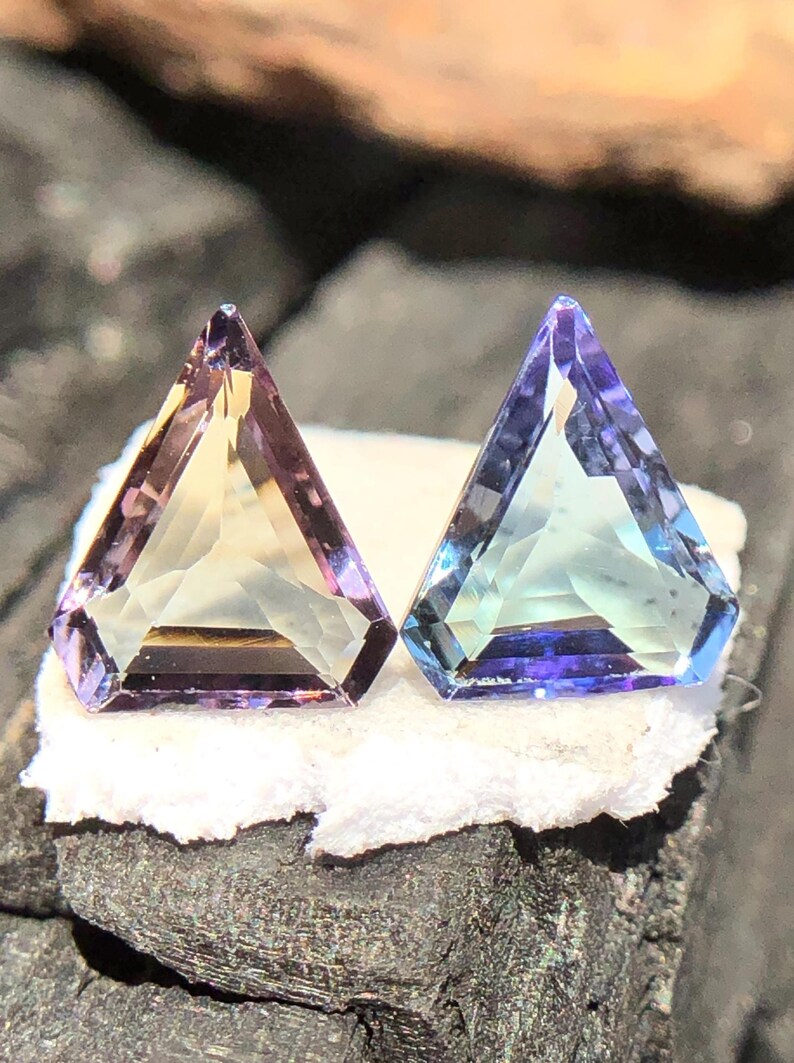 May include: Two triangular faceted gemstones, one with a purple and yellow hue and the other with a blue and green hue.