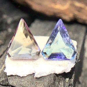 May include: Two triangular faceted gemstones, one is a pale yellow-green with a hint of purple, the other is a light blue with a hint of green.