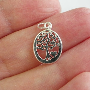 May include: Silver charm in the shape of a tree of life with a heart at the base. The charm is oval shaped and has a delicate design.