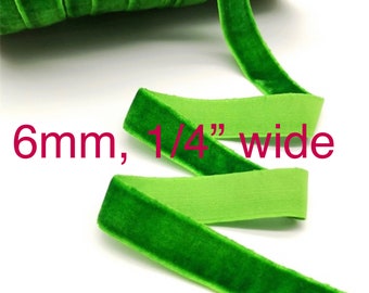 May include: A spool of vibrant green velvet ribbon with a soft, textured pile on one side and a smooth, flat backing. The ribbon measures 6mm, 1/4" wide, as indicated by the text printed directly over the image, showing a consistent width.