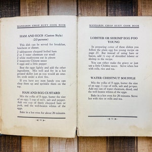 Pu&ograve; includere: Pagine aperte di un vecchio libro di cucina con ricette per Ham and Eggs e Lobster or Shrimp Egg Foo Young. Il testo &egrave; in inglese, con istruzioni ed elenchi di ingredienti. Il libro &egrave; aperto su una superficie di legno.