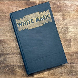 May include: A dark blue hardcover book with the title "WHITE MAGIC" in gold lettering on the front cover.