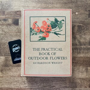 May include: A hardcover book titled The Practical Book of Outdoor Flowers by Richardson Wright, featuring a tan cover with a red border and a central illustration of orange flowers with green leaves, accompanied by a small black rectangular card.