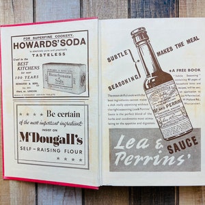 Pode incluir: Um livro de cozinha vintage aberto com dois an&uacute;ncios. A p&aacute;gina da esquerda apresenta uma caixa branca com o texto "Howards' Soda" e uma caixa menor com o texto "Bicarbonate of Soda". A p&aacute;gina da direita apresenta uma garrafa marrom de molho Lea & Perrins com o texto "Lea & Perrins' Sauce" e "Makes the Meal Subtle Seasoning".
