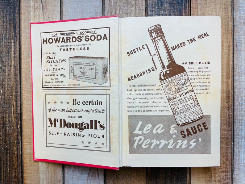 Pode incluir: Um livro de cozinha vintage aberto com dois an&uacute;ncios. A p&aacute;gina da esquerda apresenta uma caixa branca com o texto "Howards' Soda" e uma caixa menor com o texto "Bicarbonate of Soda". A p&aacute;gina da direita apresenta uma garrafa marrom de molho Lea & Perrins com o texto "Lea & Perrins' Sauce" e "Makes the Meal Subtle Seasoning".