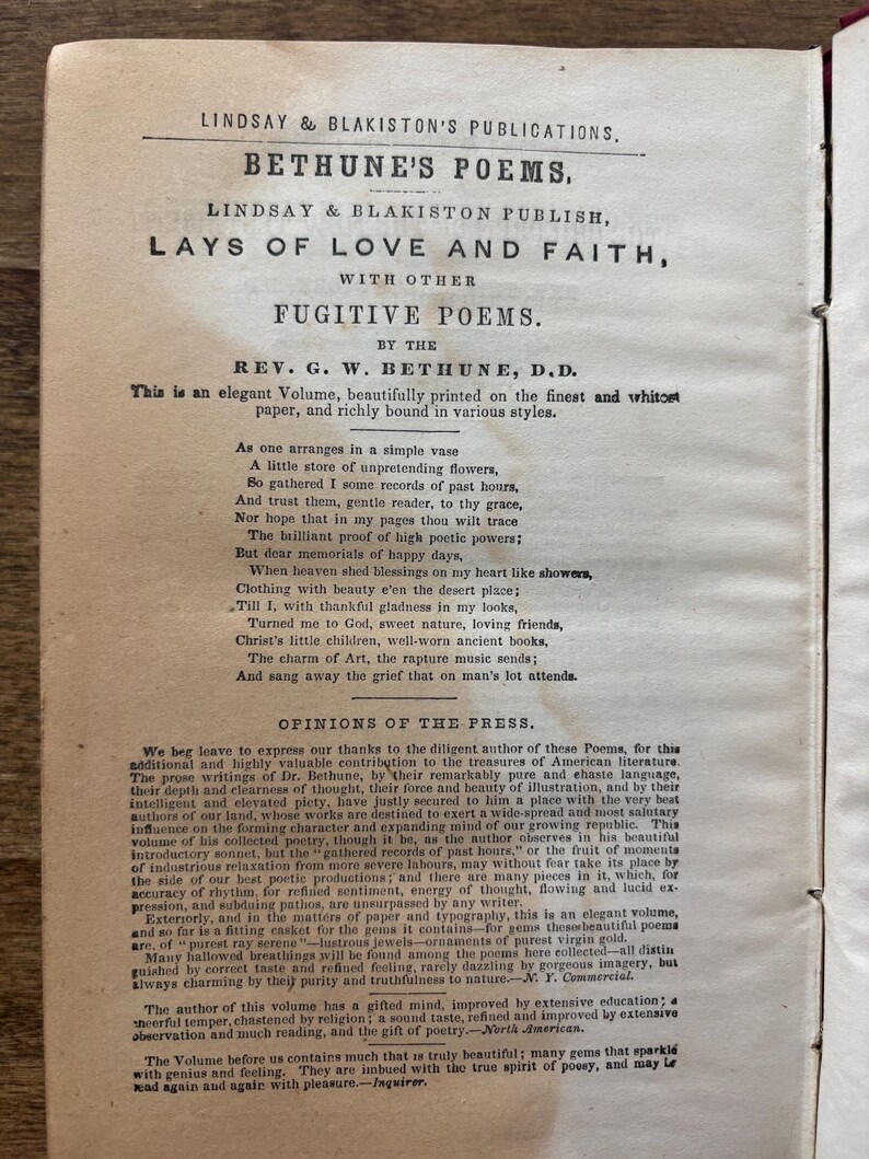 May include: An open book with the title "Bethune's Poems" by Lindsay & Blakiston. The pages display printed text, including the author's name, poem titles, and opinions from the press. The book is aged with a vintage aesthetic.