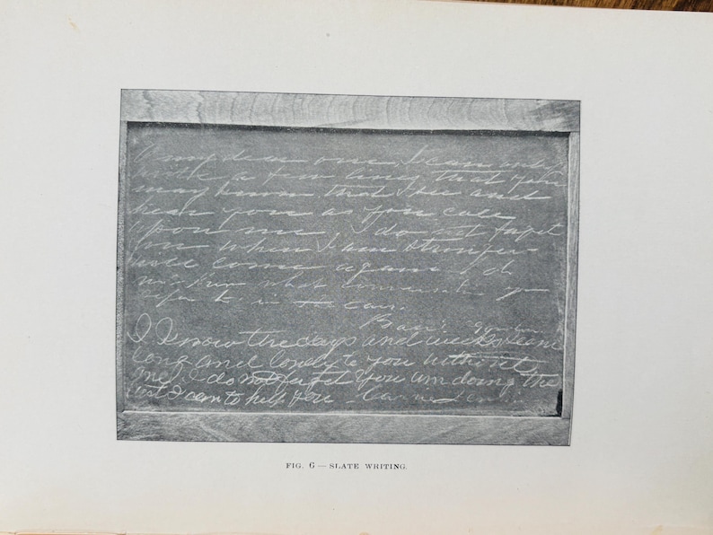 May include: A monochrome image of a slate chalkboard with handwritten text in white chalk. The chalkboard is framed with a wooden border. The text is a handwritten letter. The bottom of the image has the text "FIG. G - SLATE WRITING."