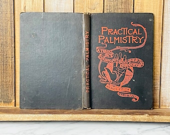 May include: A black hardcover book titled "Practical Palmistry: A Treatise on Cheirosophy Based Upon Actual Experiences" by Henry Frith. The book cover features a red illustration of a hand with a swirling design.
