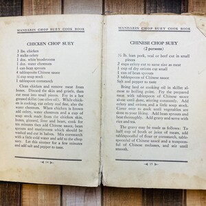 Pu&ograve; includere: Pagine aperte di un vecchio libro di cucina con ricette per Chicken Chop Suey e Chinese Chop Suey. Il libro, intitolato "Mandarin Chop Suey Cook Book", &egrave; appoggiato su una superficie di legno.