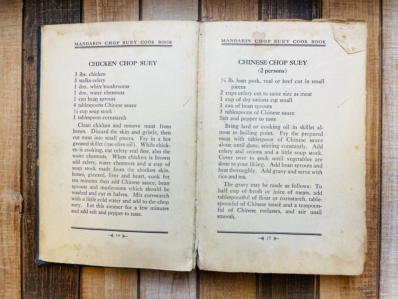 Pu&ograve; includere: Pagine aperte di un vecchio libro di cucina con ricette per Chicken Chop Suey e Chinese Chop Suey. Il libro, intitolato "Mandarin Chop Suey Cook Book", &egrave; appoggiato su una superficie di legno.