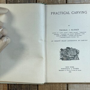Pode incluir: Um livro antigo intitulado "Practical Carving" de Thomas J. Murrey. A capa do livro apresenta uma ilustra&ccedil;&atilde;o em preto e branco de uma pessoa a esculpir um assado.