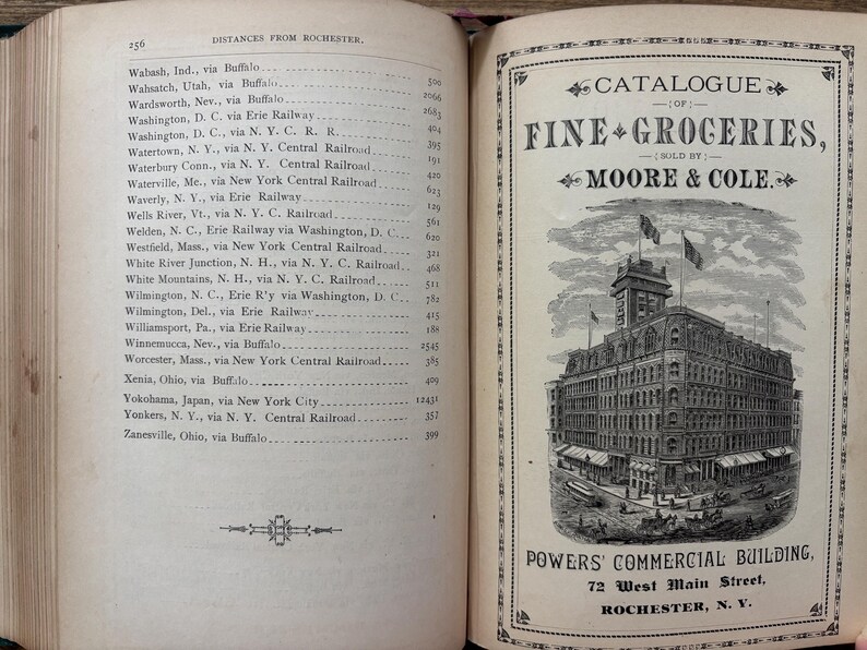 May include: An open book with a page titled "DISTANCES FROM ROCHESTER" and a catalog for "FINE GROCERIES" sold by Moore & Cole. The catalog features an illustration of the Powers Commercial Building in Rochester, N.Y.