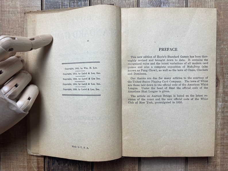 Puede incluir: Un primer plano de la p&aacute;gina de prefacio de un libro con el t&iacute;tulo "Prefacio" y texto que describe el contenido y las revisiones del libro. El texto menciona la inclusi&oacute;n en el libro de reglas para varios juegos de cartas, incluyendo Mah-Jong, ajedrez, damas y domin&oacute;. El texto tambi&eacute;n reconoce las contribuciones de United States Playing Card Company y la American Whist League.