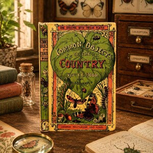 May include: A vintage hardcover book titled Common Objects of the Country by Rev. J.G. Wood. The yellow cover features a large green leaf illustration, various insects, and butterflies. The text reads One Shilling, with Twelve Plates and George Routledge and Sons.