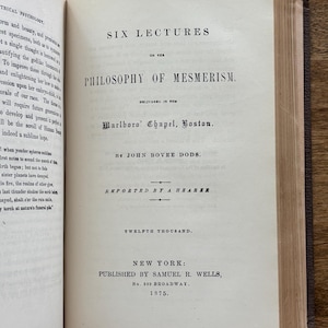 Puede incluir: Libro abierto con el t&iacute;tulo "SIX LECTURES ON THE PHILOSOPHY OF MESMERISM" de John Bovee Dods, publicado en Nueva York en 1875. Las p&aacute;ginas est&aacute;n envejecidas, con texto visible y una cubierta azul oscuro.