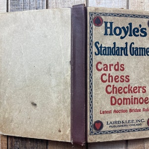 Puede incluir: Un libro vintage titulado "Hoyle's Standard Games" con una encuadernaci&oacute;n marr&oacute;n y una cubierta de color beige. El libro presenta una lista de juegos, incluyendo cartas, ajedrez, damas y domin&oacute;. El libro est&aacute; publicado por Laird & Lee, Inc. en Chicago.