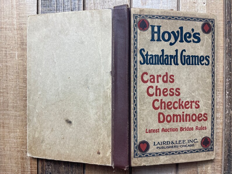 Puede incluir: Un libro vintage titulado "Hoyle's Standard Games" con una encuadernaci&oacute;n marr&oacute;n y una cubierta de color beige. El libro presenta una lista de juegos, incluyendo cartas, ajedrez, damas y domin&oacute;. El libro est&aacute; publicado por Laird & Lee, Inc. en Chicago.