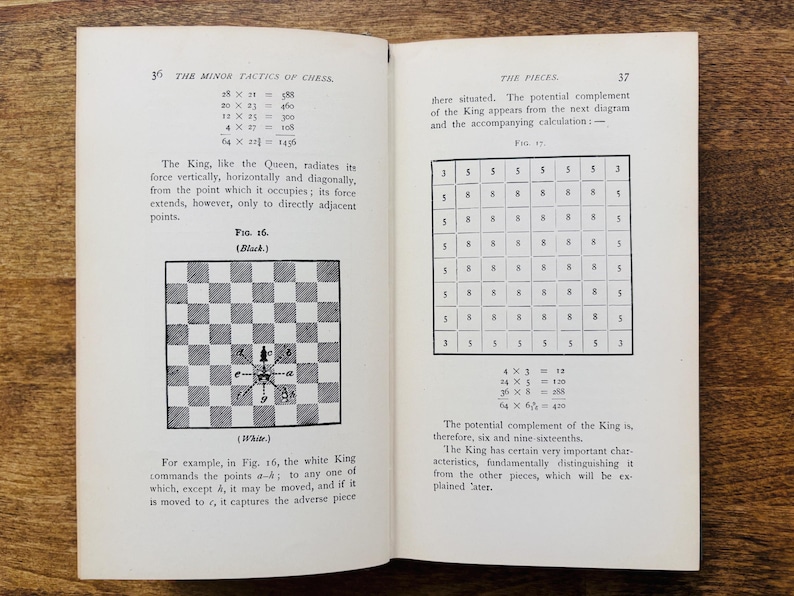 May include: Open book with pages displaying chess diagrams and text. The left page features a black and white chessboard diagram with arrows. The right page shows a grid of numbers. The book is open on a wooden surface.