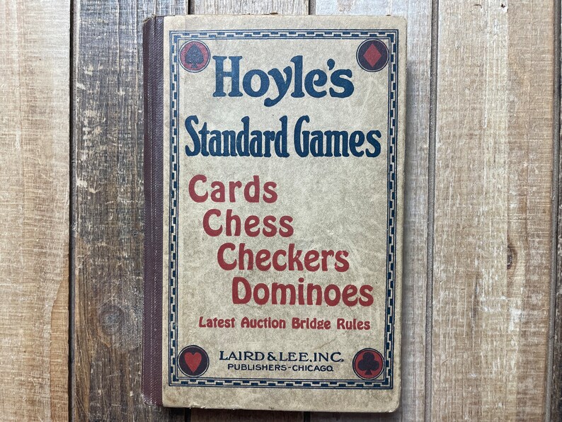 Puede incluir: Un libro vintage titulado "Hoyle's Standard Games" con una cubierta marr&oacute;n y texto rojo y azul. El libro presenta una lista de juegos, incluyendo cartas, ajedrez, damas y domin&oacute;. El libro tambi&eacute;n incluye el texto "Latest Auction Bridge Rules" y la informaci&oacute;n del editor "LAIRD & LEE, INC. PUBLISHERS-CHICAGO".