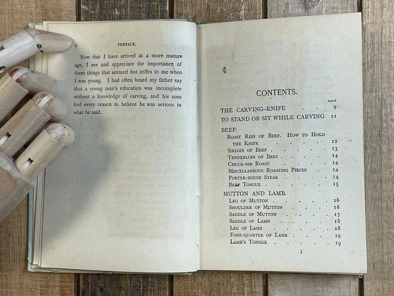 Pode incluir: Um livro antigo com capa branca e texto preto. O t&iacute;tulo do livro &eacute; "The Carving-Knife" e o conte&uacute;do inclui uma lista de diferentes cortes de carne, como carne bovina, carneiro e cordeiro.