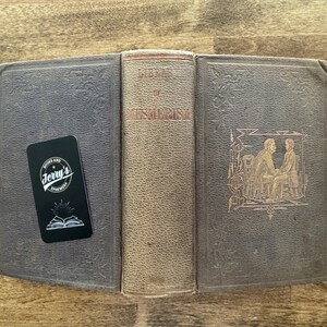 Puede incluir: Un libro antiguo abierto con una cubierta desgastada y texturizada, con el t&iacute;tulo "Library of Esoteric". Una tarjeta de visita negra con el texto "Jerry's Ephemera" descansa sobre el libro. La cubierta del libro es de color gris oscuro.