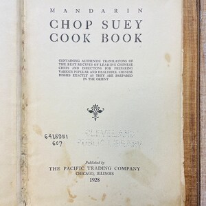 Pu&ograve; includere: Libro aperto intitolato "Mandarin Chop Suey Cook Book" con testo sulle ricette cinesi. Pubblicato da The Pacific Trading Company nel 1928. Il libro &egrave; invecchiato con usura visibile e le parole "Cleveland Public Library" sono visibili.