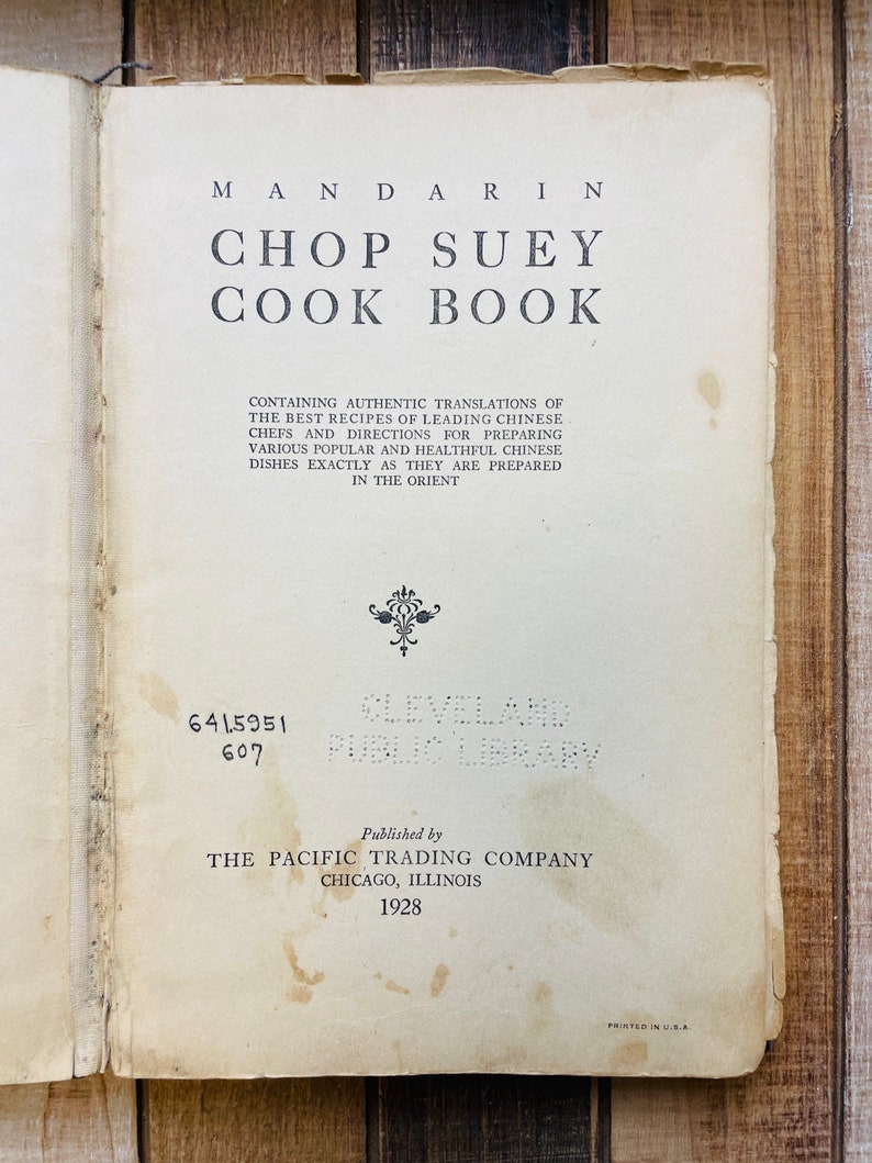 Pu&ograve; includere: Libro aperto intitolato "Mandarin Chop Suey Cook Book" con testo sulle ricette cinesi. Pubblicato da The Pacific Trading Company nel 1928. Il libro &egrave; invecchiato con usura visibile e le parole "Cleveland Public Library" sono visibili.