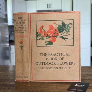 May include: A tan hardcover book titled The Practical Book of Outdoor Flowers by Richardson Wright. The cover features a rectangular illustration of orange flowers with green leaves, a red border, and black text. The spine includes the title and author.