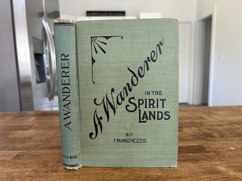 May include: An antique book titled "A Wanderer in the Spirit Lands" by Franchezzo. The book has a light green cover with black lettering and a decorative sunburst design. The spine reads "A Wanderer".