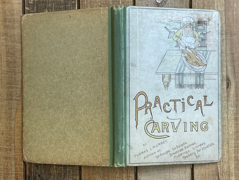 Pode incluir: Um livro vintage intitulado "Practical Carving" de Thomas J. Murrey, autor de "50 Soups, 50 Salads". A capa apresenta um desenho de linha de uma pessoa cortando um peru em uma mesa.