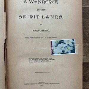 May include: Open book with the title "A Wanderer in the Spirit Lands" by Franchezzo. The cover is a light brown color with black text. A stamp with white flowers is affixed to the page. Published in Chicago in 1901.