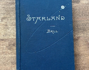 Puede incluir: Un libro antiguo de tapa dura azul marino titulado "Starland Ball". La portada presenta el título en una fuente estilizada, con un gráfico de un planeta y estrellas. El lomo del libro es visible en el lado izquierdo.