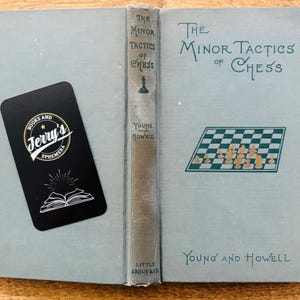 May include: Open book titled "The Minor Tactics of Chess" with a light blue cover and a chess board illustration. A black bookmark with "Jerry's Ephemera" logo is on the left. The book is by Young and Howell.